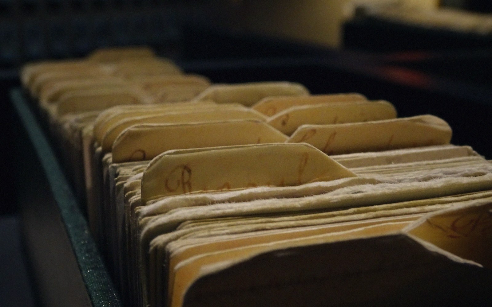 Rows of aged index cards with handwritten labels in a wooden filing drawer