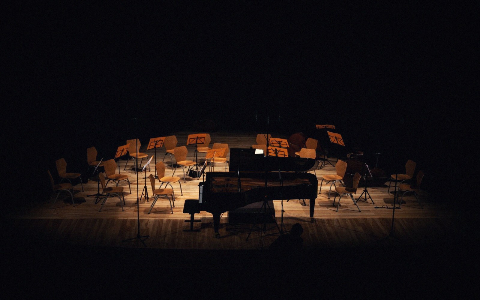 Empty chairs and music stands encircle a grand piano on a dimly lit stage
