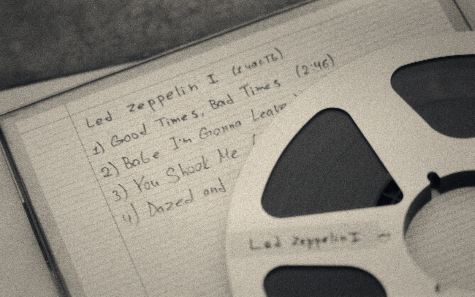 A reel-to-reel tape labeled Led Zeppelin I resting on a handwritten tracklist notebook