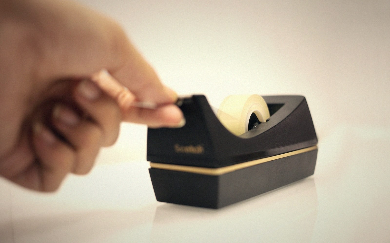 A hand reaches toward a black tape dispenser holding a roll of tape