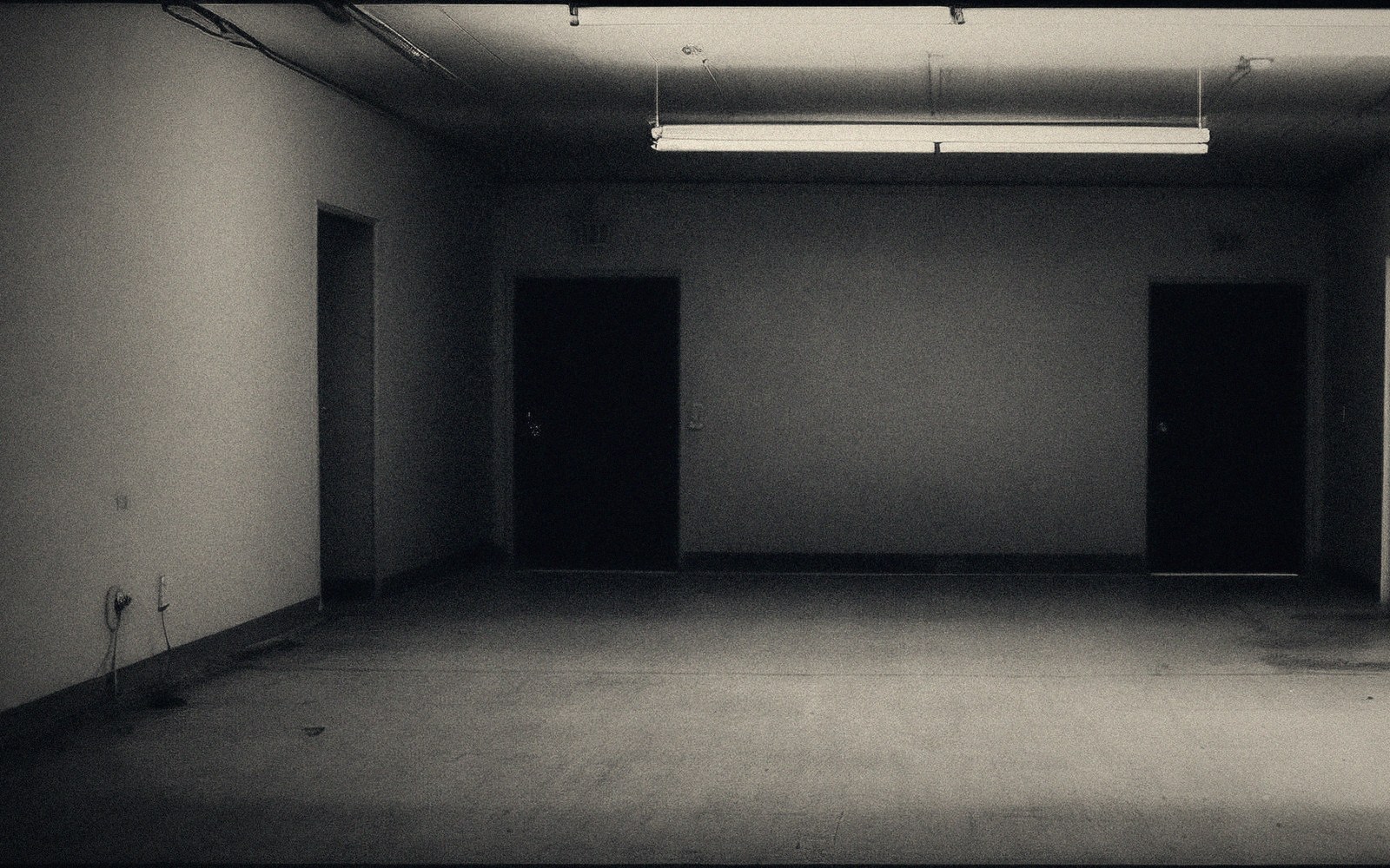 An empty room lit by a single fluorescent tube, with dark doorways along the far wall