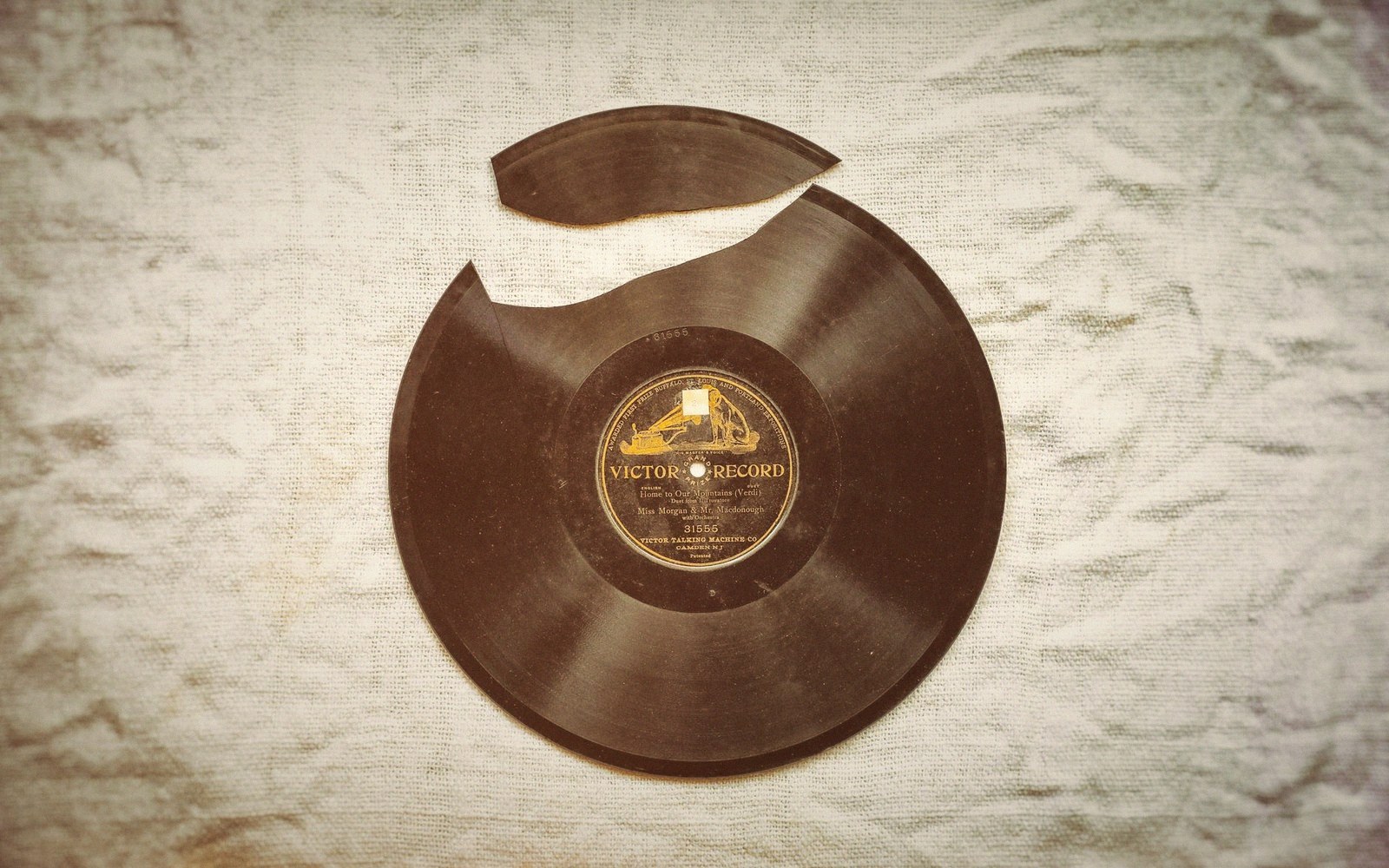 A stack of shellac 78s in worn paper sleeves under one lamp