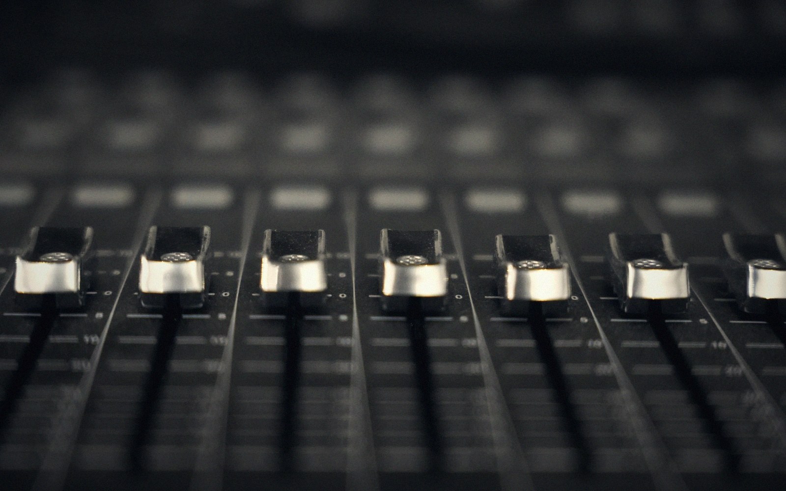 A mixing desk with faders lit from one side in the dark